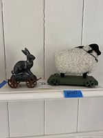 Photo of black metal rabbit pull toy and white wool sheep pull toy on shelf.