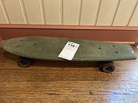 Full side view of the vintage skateboard on wooden floor showing green deck with scratches and pre-drilled holes.
