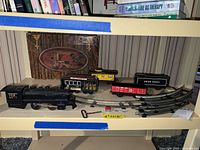Photo showing the full vintage train set with the black steam locomotive, four tin cars including a union pacific tender, and eight curved track pieces arranged on a shelf.