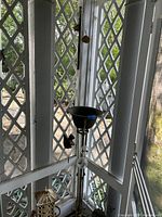 Overall view of metal wind chime stand with black bowl top and hanging glass and bird ornaments on screened porch