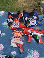 Overall lot with two vests, goggles, three blasters and loose darts displayed
