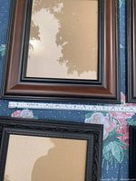 two brown wood-tone frames and two black ornate frames on table with ruler for scale