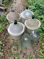 Six carboys on garden path, four in baskets, two bare glass