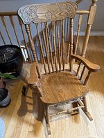 Full view of the wooden rocking chair showing carved top rail, spindled backrest and contoured wooden seat.