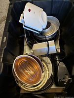 Top-down view of the black storage bin showing a white sandwich press, metal cake pans, electric can opener, and vintage warmer tray.