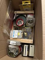 Box with assorted small hardware items including screws, nails, fasteners, sanding sponge, and packaging visible from above.