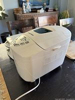 Side angle view of the white bread machine showing the ventilation slots and control panel area.