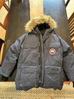 Front view of navy parka with coyote fur trimmed hood, visible Canada Goose Arctic Program patch and multiple pockets