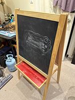 Front and angled side view of wooden frame chalkboard with chalk tray and chalk drawing on the surface