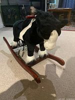 Front-side angle of the black and white plush rocking horse showing the horse's head, mane, and wooden rockers with minor scratches.