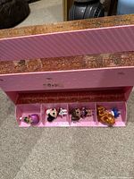 Pink glittered storage holder open showing four LOL dolls inside, different sizes and styles with colorful hair
