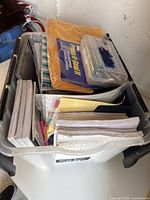 View of the plastic bin containing packs of lined paper, binders, manila envelopes, and a compartment box on top.