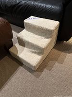 Three-step dog stairs next to a black leather couch and brown chair, showing general shape and condition of fabric cover.