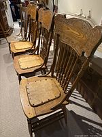 Four vintage wooden press back chairs in a row, three matching with carved backs and cushioned seats, one different with plain wooden seat