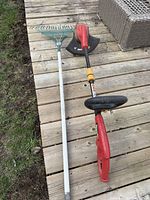 Homelite red electric corded string trimmer and a metal garden rake with wooden handle lying on wooden deck, showing general condition and details of both items.