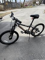 Side view of the black and gray kids bike showing frame, tires, pedals, saddle, and chain mechanism.
