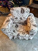 Front view of upholstered kids rocking lounger chair showing paisley and floral fabric and ruffled base skirt, with visible wear and dirt on fabric.