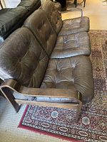 Front perspective showing tufted dark brown leather cushions and wooden frame