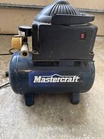 Front view of Mastercraft air compressor showing brand logo and aged surface with minor scratches and rust.