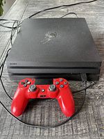 Black PS4 Pro console and red controller on table