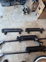 Overhead image of four black horizontal mounting bars for ski/snowboard roof rack on concrete floor. Shows peeling paint and signs of surface rust.