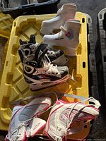 Three pairs of kids ice skates arranged in a yellow plastic bin, showing overall condition and styling