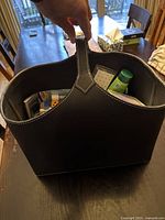 Front view of the black leather tote bag showing the handle and some visible contents inside, including stationery and household items.