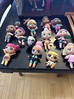 Top view of 13 LOL dolls arranged on a black surface, showing a variety of hair colors and outfits.