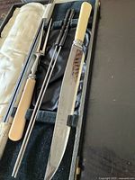 Photo showing vintage carving knife, fork, two sharpening steels housed in black case with satin lining.