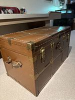 Photo of vintage metal steamer trunk closed, showing brass hardware and rivets on edges
