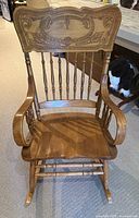 Front view of wooden rocking chair showing carved backrest, spindle supports, sculpted seat and armrests.