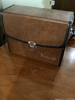 Closed brown vintage style Bushnell carry case with shoulder strap and metal clasp lock on front