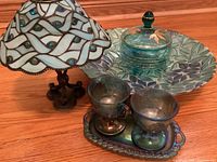 Photo showing stained glass candle lamp, large decorative plate, covered glass dish, blue glass goblets on tray, and creamer.