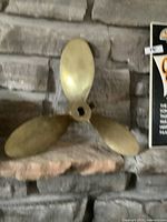 Overall view of the three-bladed solid brass boat propeller resting on stone background.