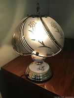 Front angle showing the lamp illuminated, frosted glass floral shade, and porcelain floral base.