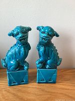 Pair of turquoise ceramic Foo Dogs seated on square bases on wooden surface against white background