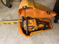 Top view of the Pioneer Partner 600 chainsaw inside its yellow carrying case, showing the chainsaw body, protective bar cover, and case open on the ground.