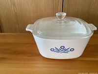 White rectangular Corelle casserole dish with blue floral pattern and matching clear glass lid, shown on wood surface background.