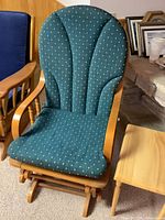 Photo showing padded glider rocking chair with teal fabric and small wood side table beside it.