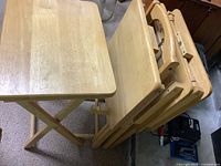 Set of four light hardwood folding TV dinner tables shown standing folded next to one unfolded table.