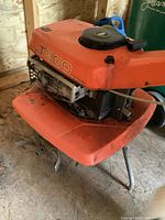 Side view of orange roto-tiller showing engine housing, air filter cover marked T300, lower tine guard and front support legs