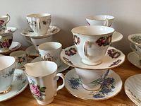 Multiple porcelain teacups and saucers arranged on a surface showing various floral patterns and gold trim detailing.