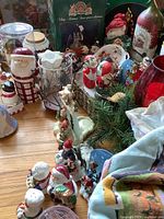 Full view of lot showing various Christmas figurines, greenery, glassware, and textiles arranged on floor surface.