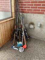 Group of fishing rods leaning against a wall with accessories at the base