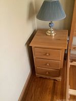 Front view of oak nightstand showing three drawers and matching lamp on top