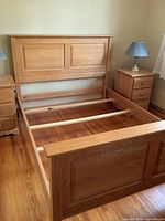 Full view of oak queen bed frame assembled in room, showing headboard, footboard, side rails and slats