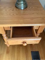 Top and front view of oak side table showing small drawer partially open, lamp base on top, and wood grain.