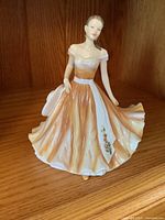 Front view of the ceramic figurine showing the woman in an orange dress with white and floral details, posed holding out her skirt.