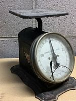 Front angled view of vintage Landers, Frary & Clark farm scale showing black metal body, square platform on top, and round dial face with numbers up to 24.