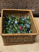 Photo shows a full rectangular woven basket filled with assorted glass marbles of various colors and patterns.